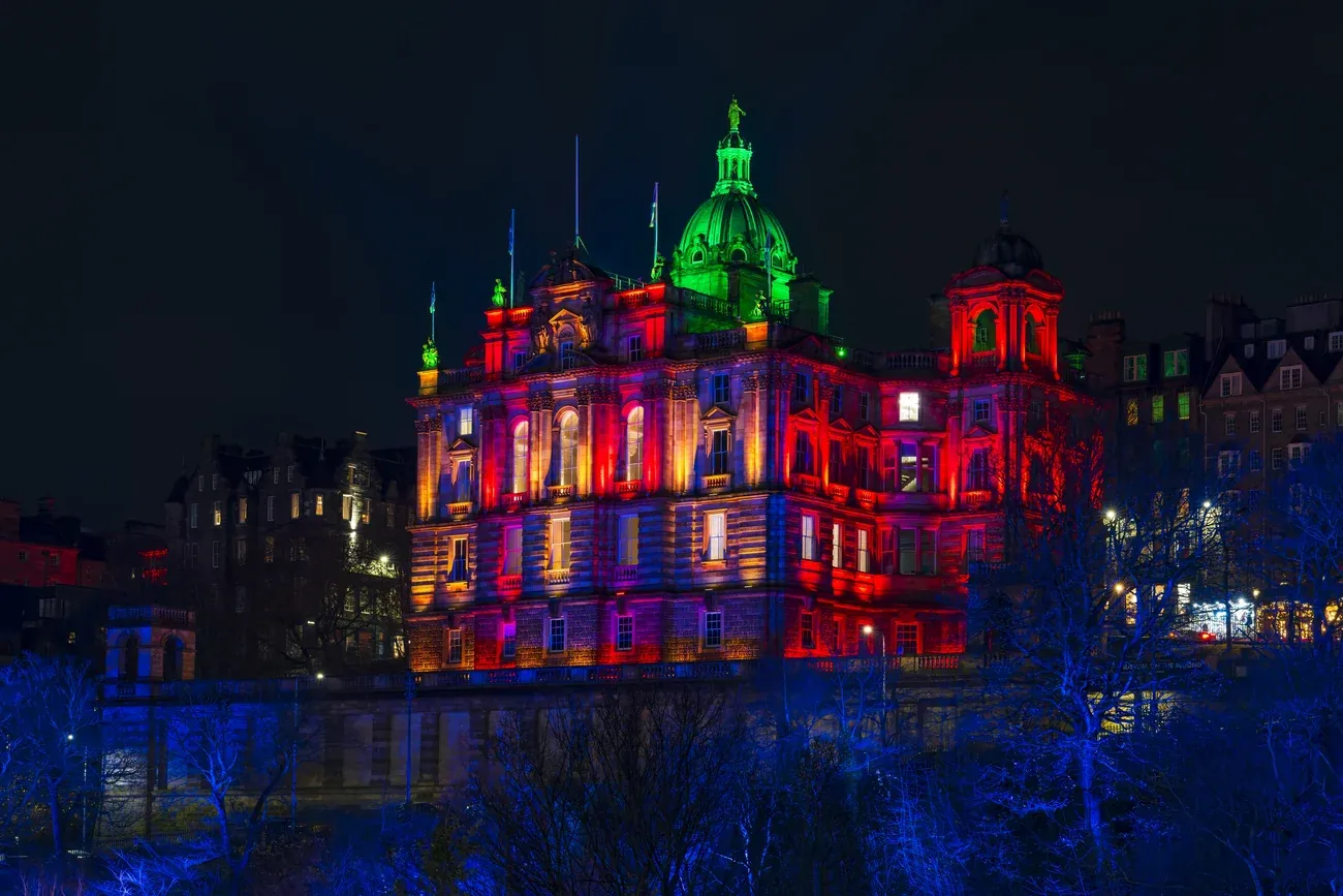 The Bank of Scotland headquarters on The Mound in Edinburgh lit in red and green at night, above blue-lit trees