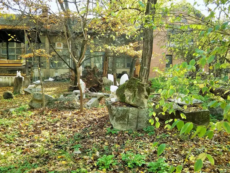 Plaster casts and stone fragments scattered among trees in the Epreskert garden of the Hungarian University of Fine Arts in Budapest