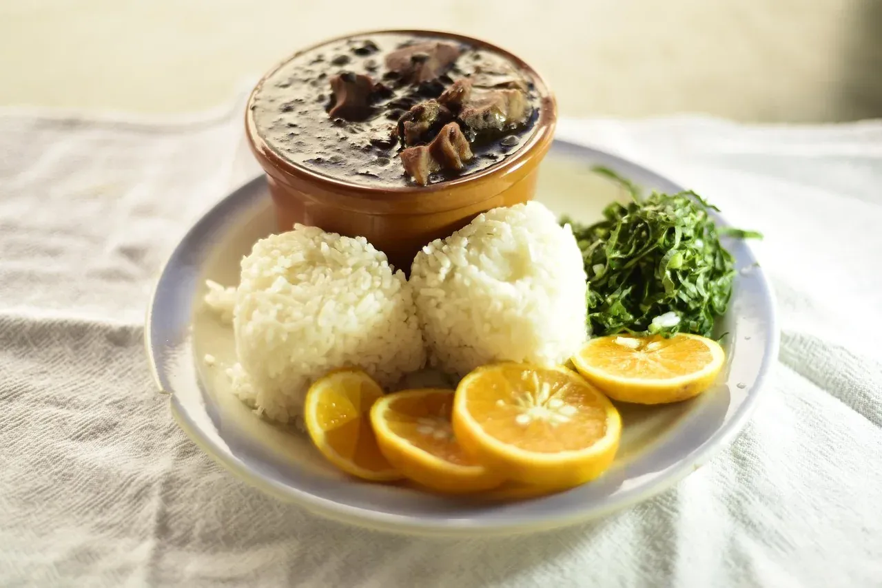 A plate of feijoada served with rice, collard greens and orange slices