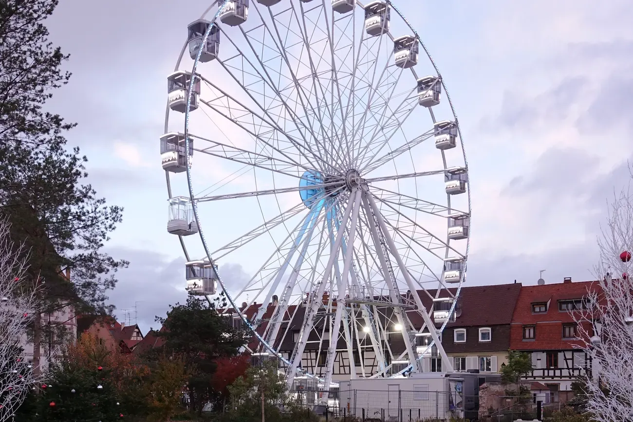 The Christmas Ferris wheel in Colmar at dusk, above trees and half-timbered houses