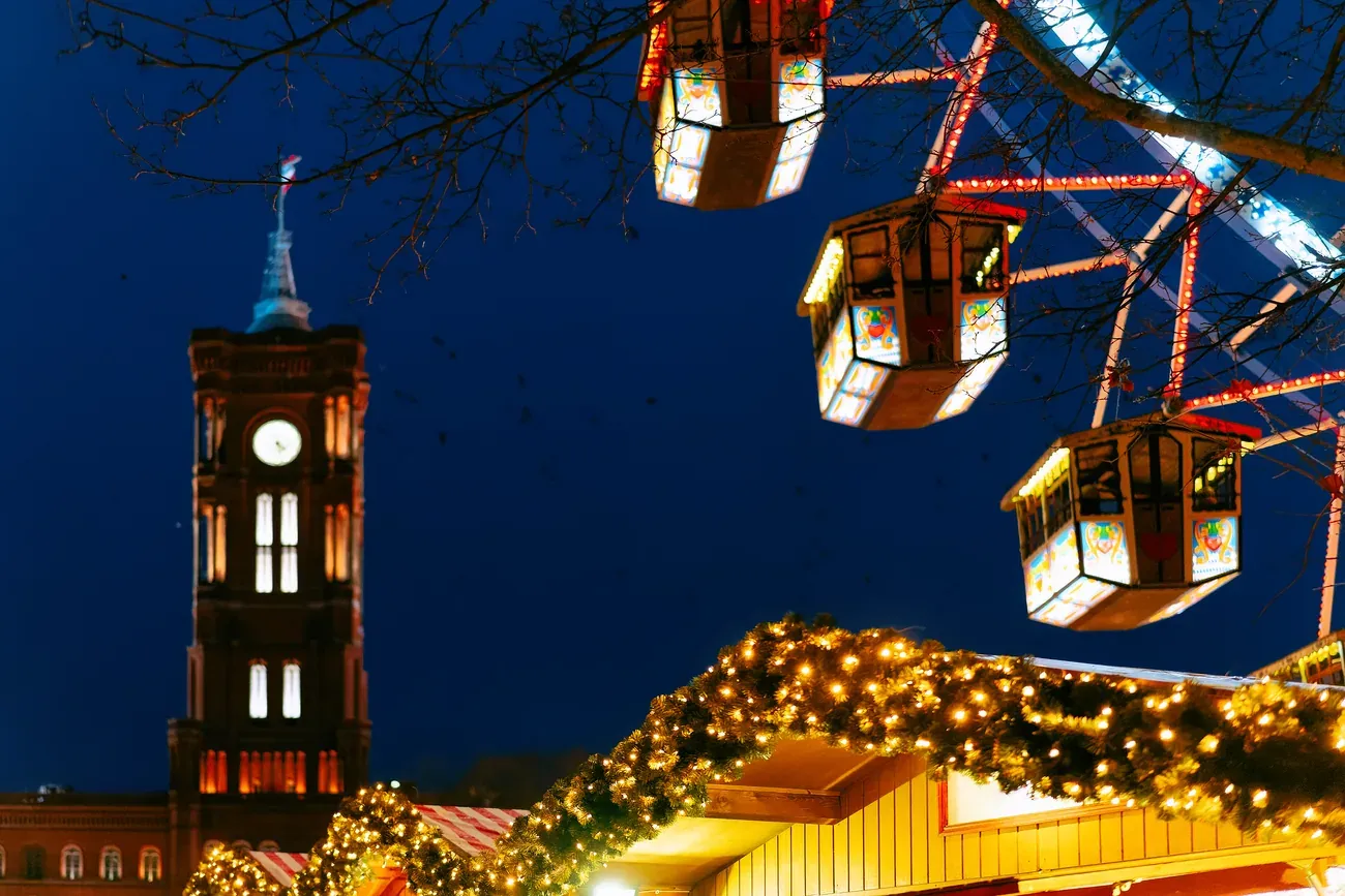 Ferris wheel gondolas and the tower of the Rotes Rathaus above the lit stalls of the Christmas market in Berlin at night