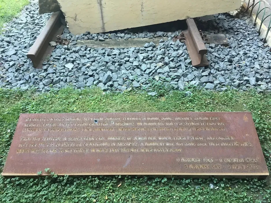 The bilingual steel plaque and broken rail of the deportation memorial at platform 16 of Santa Maria Novella station in Florence