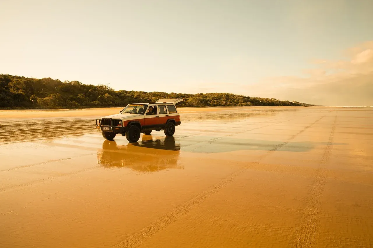 A four-wheel drive crossing the wet sand of the ocean beach on K'gari