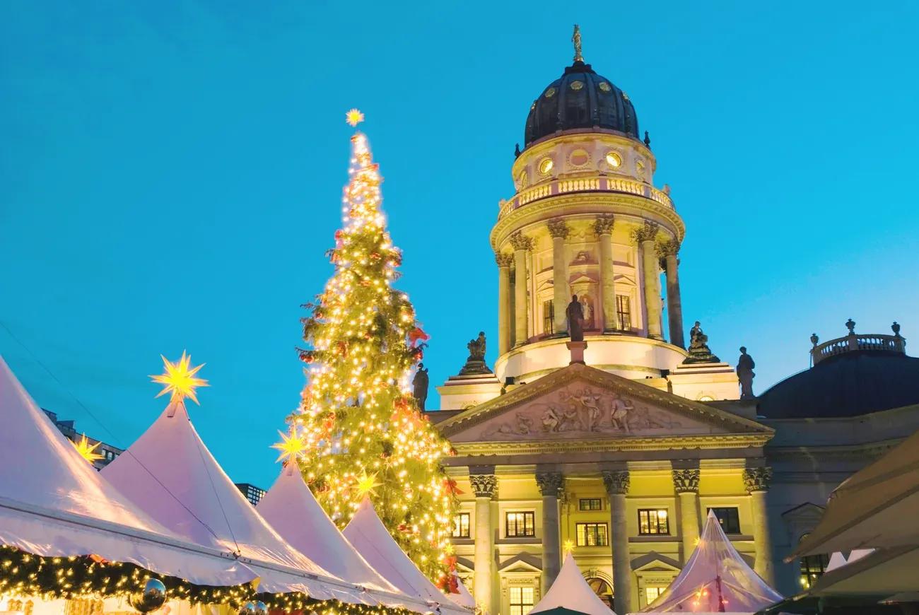 White tents and a lit Christmas tree in front of a cathedral at the Gendarmenmarkt Christmas market at night