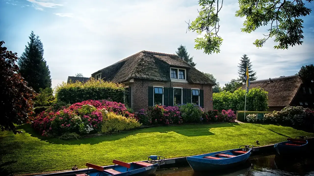 Moored boats and a thatched roof behind flowering shrubs at Giethoorn