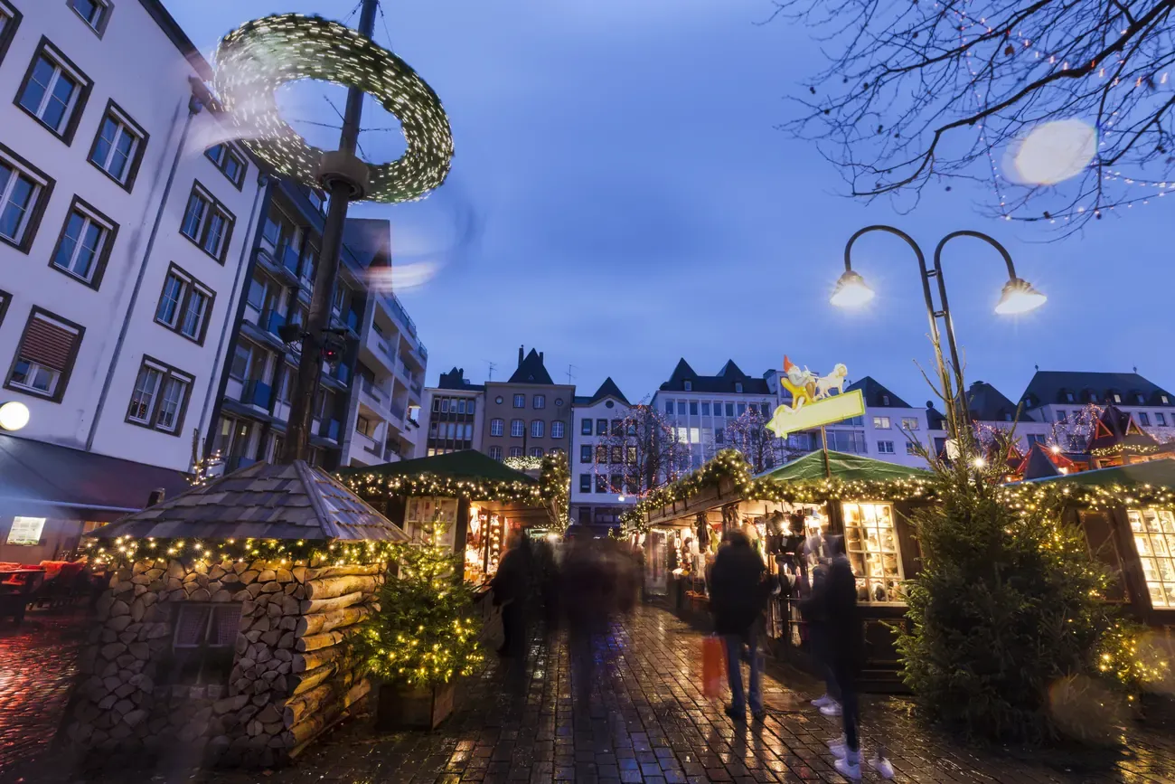 Market huts with a Heinzelmännchen sign at a Christmas market in the Old Town of Cologne at dusk