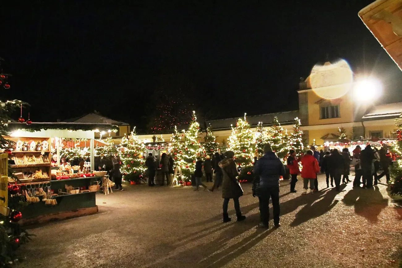 Stalls and lit Christmas trees of the Advent market in front of Hellbrunn Palace in Salzburg at night