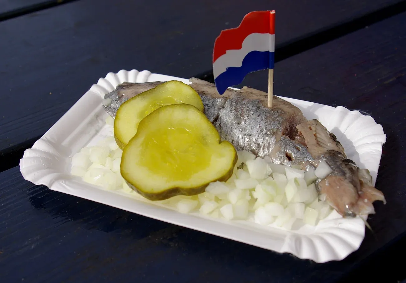 A fillet of Hollandse Nieuwe herring served on a paper tray with chopped onion and pickle