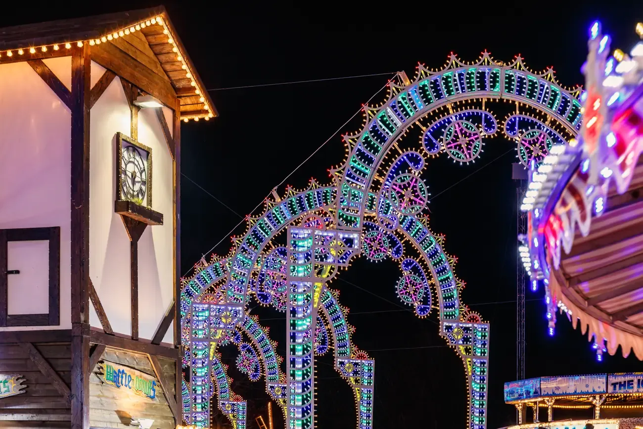 Half-timbered Bavarian-style building with a clock beside illuminated light arches at Hyde Park Winter Wonderland
