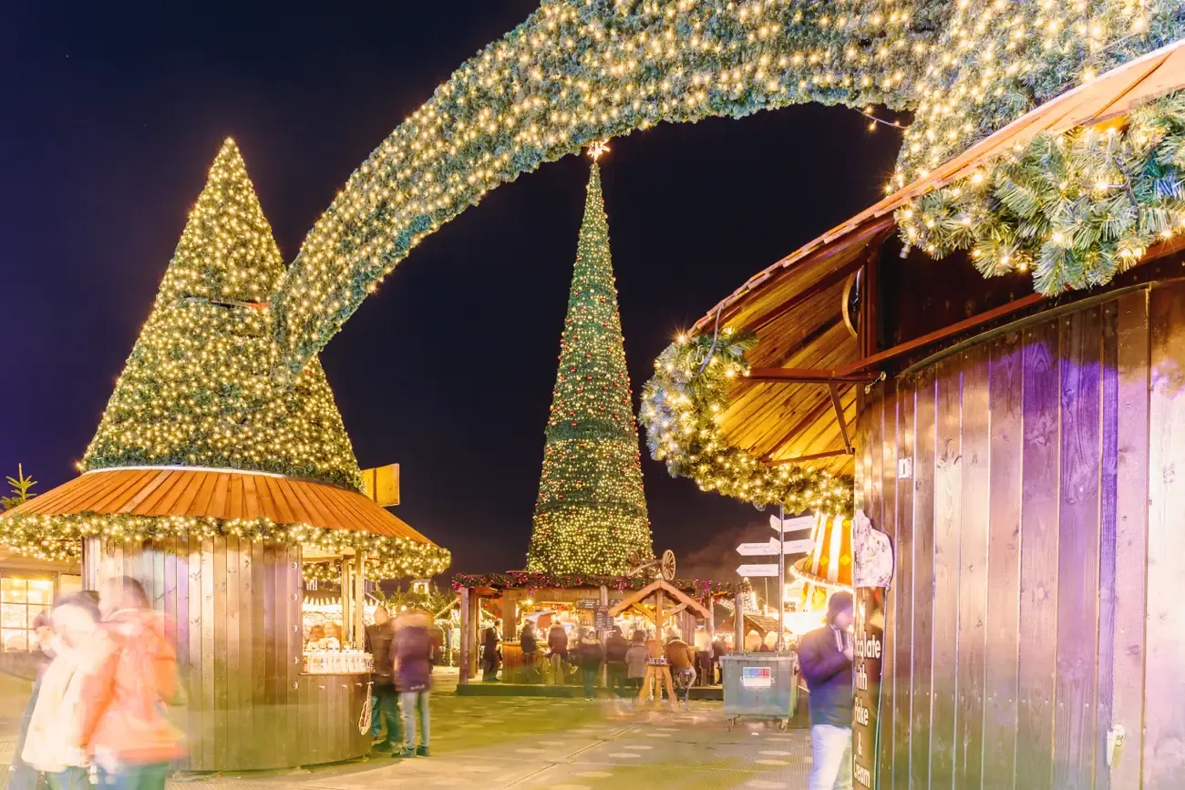 Wooden Christmas stalls with garlands and a lit Christmas tree at Hyde Park Winter Wonderland at night