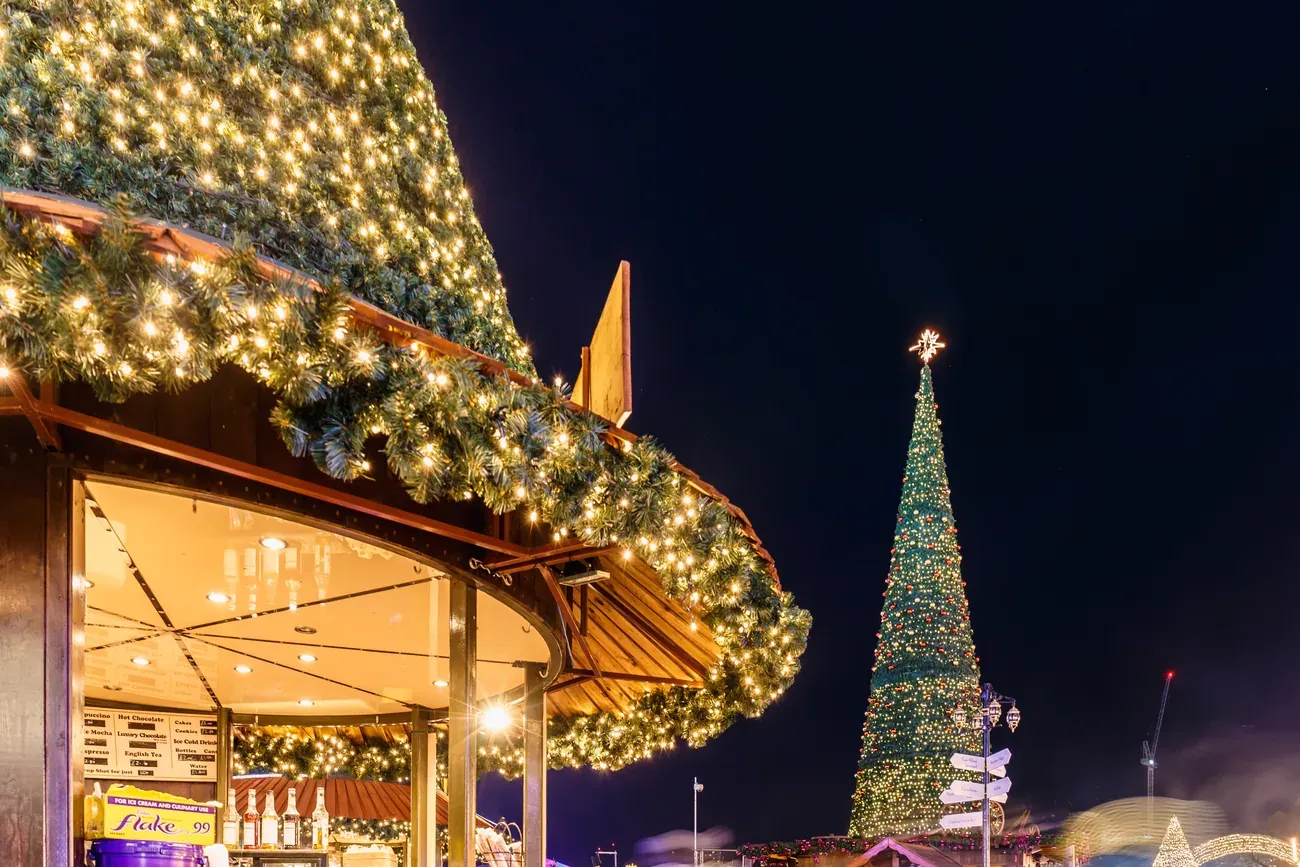 Garland-covered stall roof and an illuminated Christmas tree at Hyde Park Winter Wonderland in London