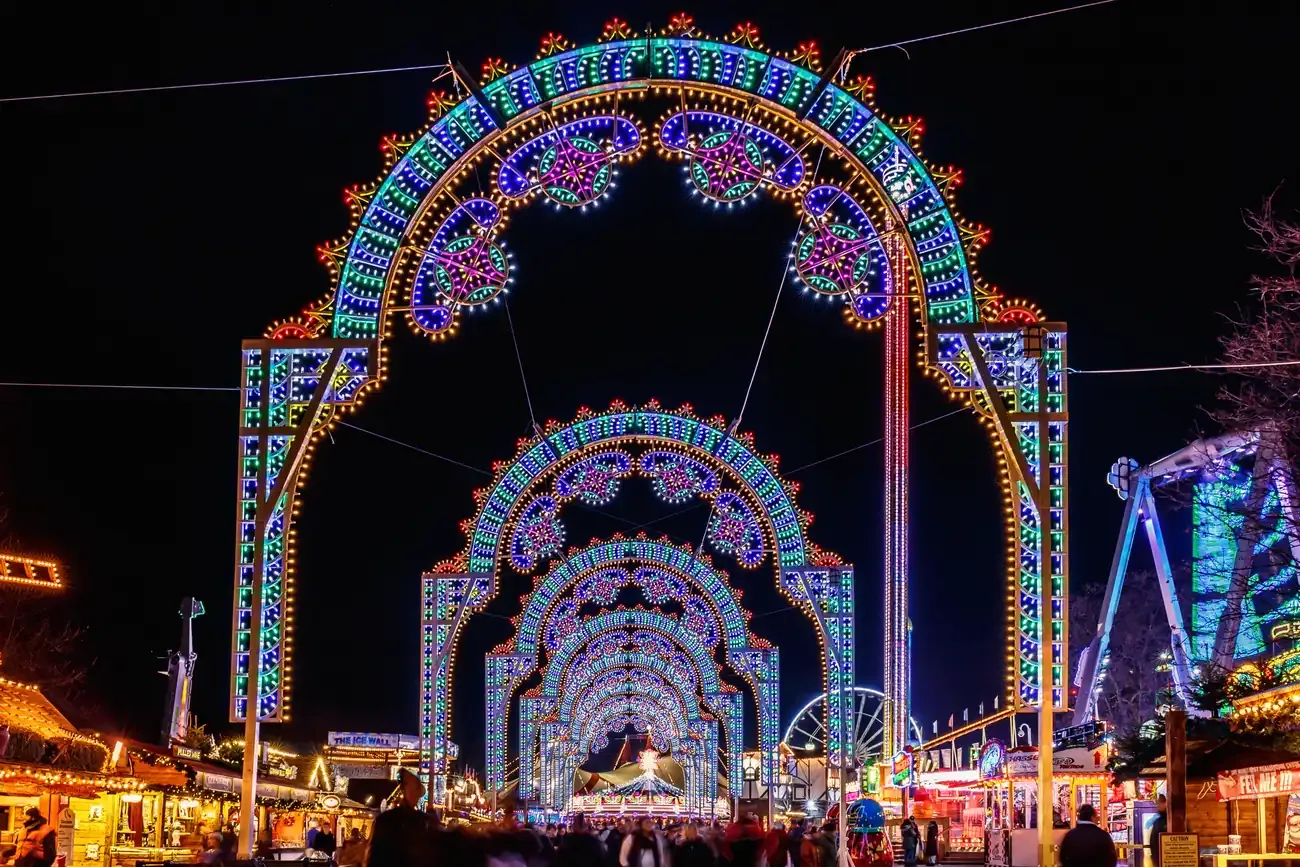 Illuminated light arches over an avenue of stalls at Hyde Park Winter Wonderland in London at night