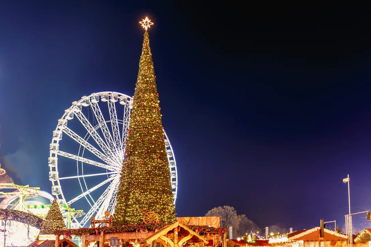 Observation wheel and a tall illuminated Christmas tree above the stalls of Hyde Park Winter Wonderland at night