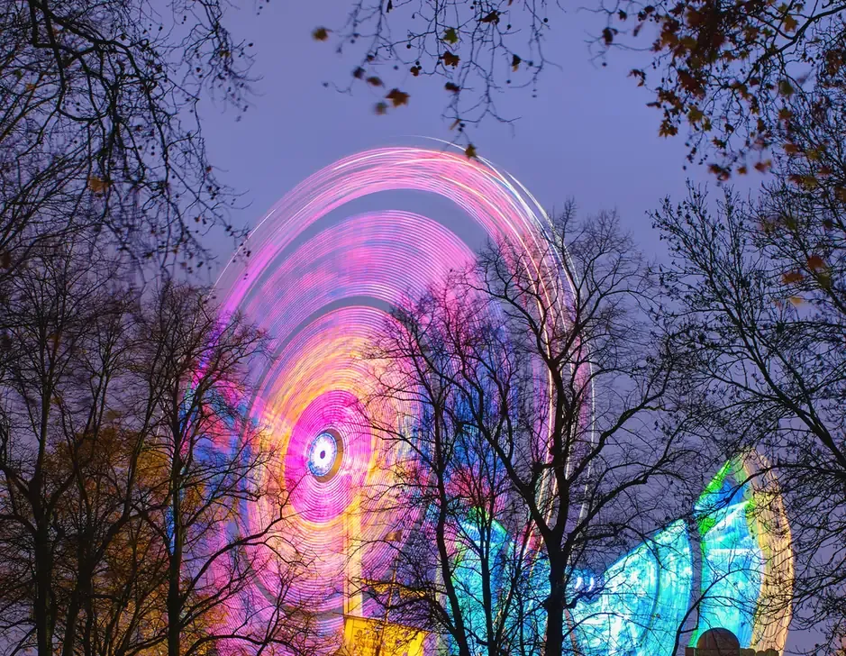Observation wheel spinning in pink and blue lights among trees at Hyde Park Winter Wonderland at night