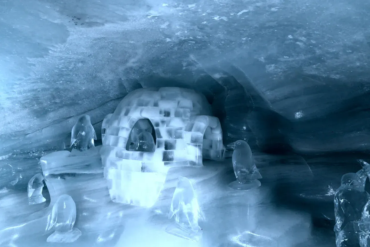 Igloo and penguin sculptures carved from ice in a blue-lit ice cave