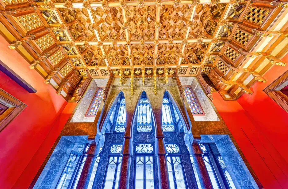 The ornate wooden ceiling and stained-glass windows inside Palau Guell in Barcelona