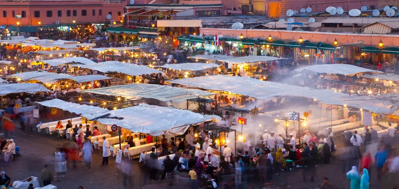 Panoramic view of the crowded food stalls at Jemaa el-Fnaa square at dusk, Marrakech.