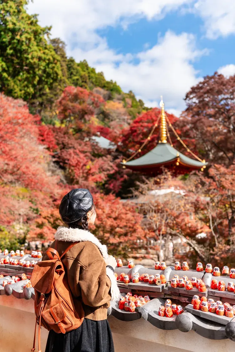 A visitor before a pagoda and rows of daruma dolls at Katsuo-ji, near Osaka