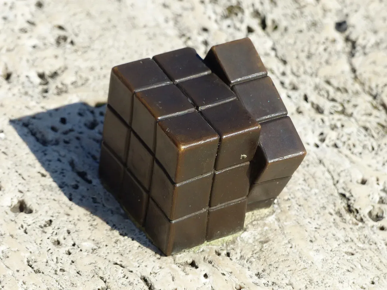Palm-sized bronze Rubik's Cube mini statue by Mihaly Kolodko on a stone ledge on the Danube embankment in Budapest
