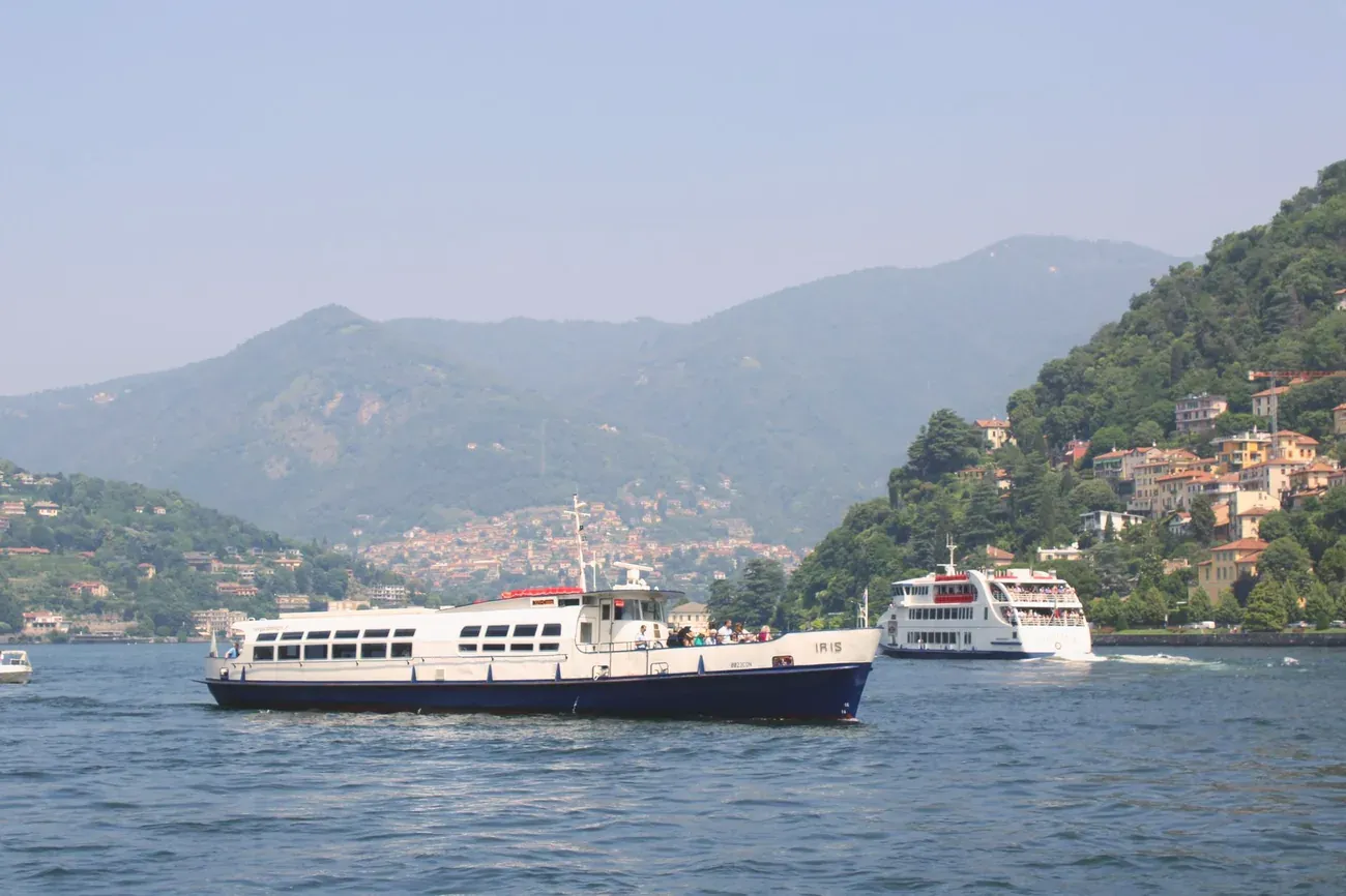 Two passenger ferries on the first basin of Lake Como with the city of Como in the distance