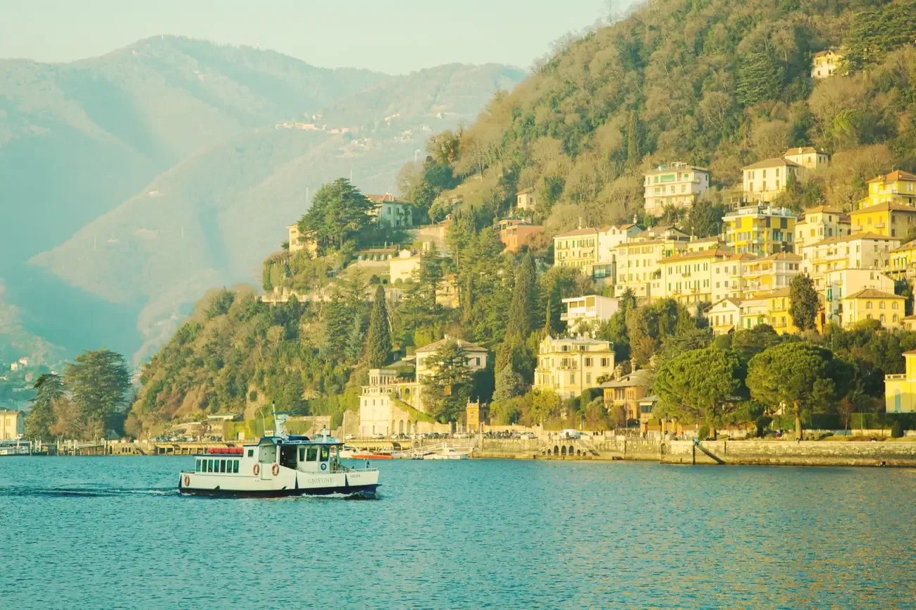 A small ferry crossing Lake Como below houses climbing the wooded hillside