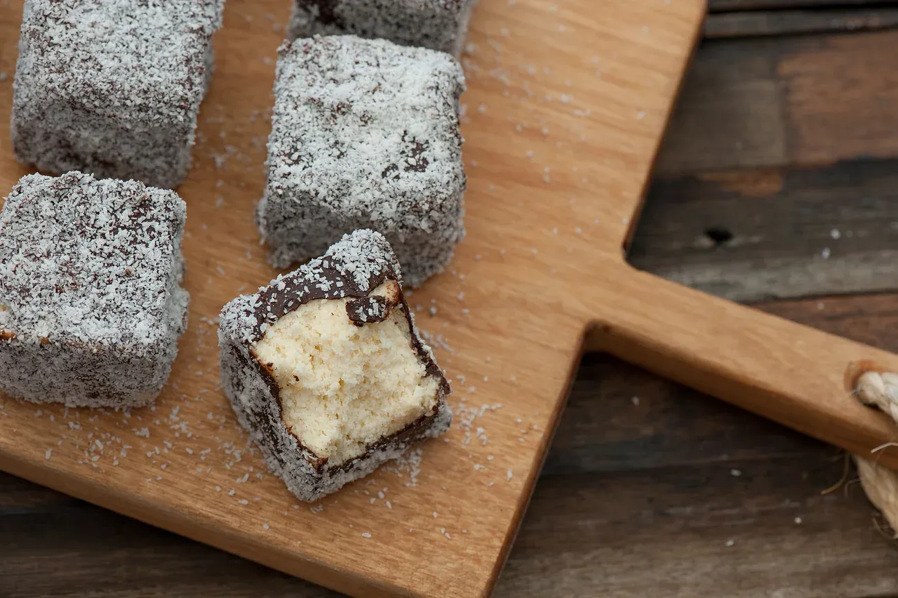 Lamingtons coated in chocolate and desiccated coconut, one cut to show the sponge
