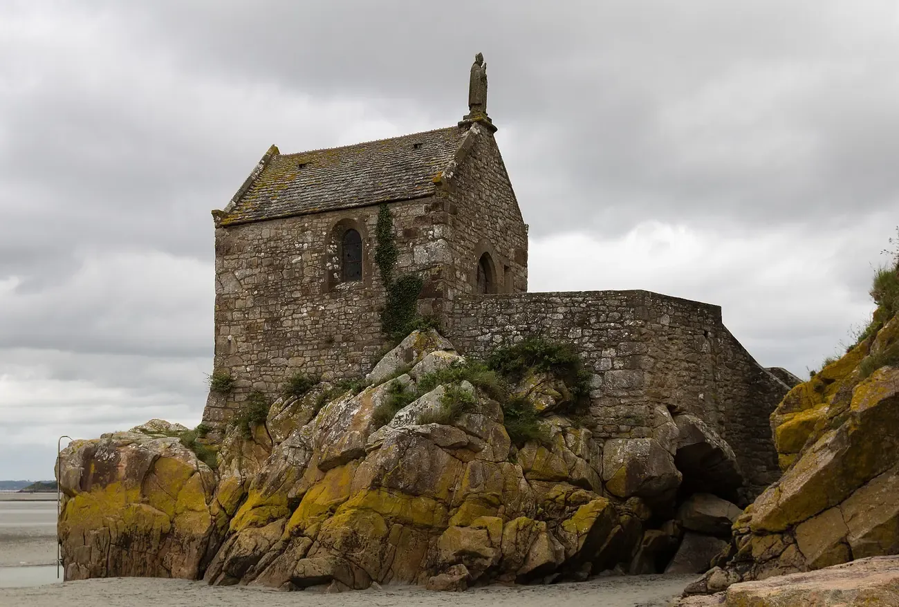 Chapelle Saint-Aubert perched on bare rock at the foot of Mont-Saint-Michel under a cloudy sky