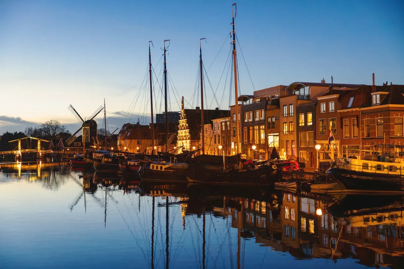 Tall ships moored on the Galgewater waterfront in Leiden at blue hour, with the De Valk windmill behind, Netherlands