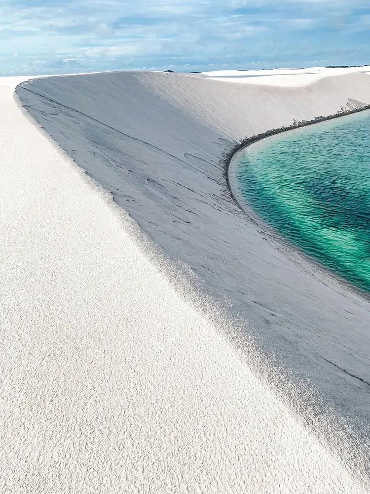 A turquoise lagoon at the foot of a white dune in Lencois Maranhenses