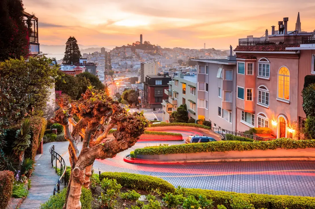 The switchback curves of Lombard Street at sunrise with Coit Tower behind in San Francisco
