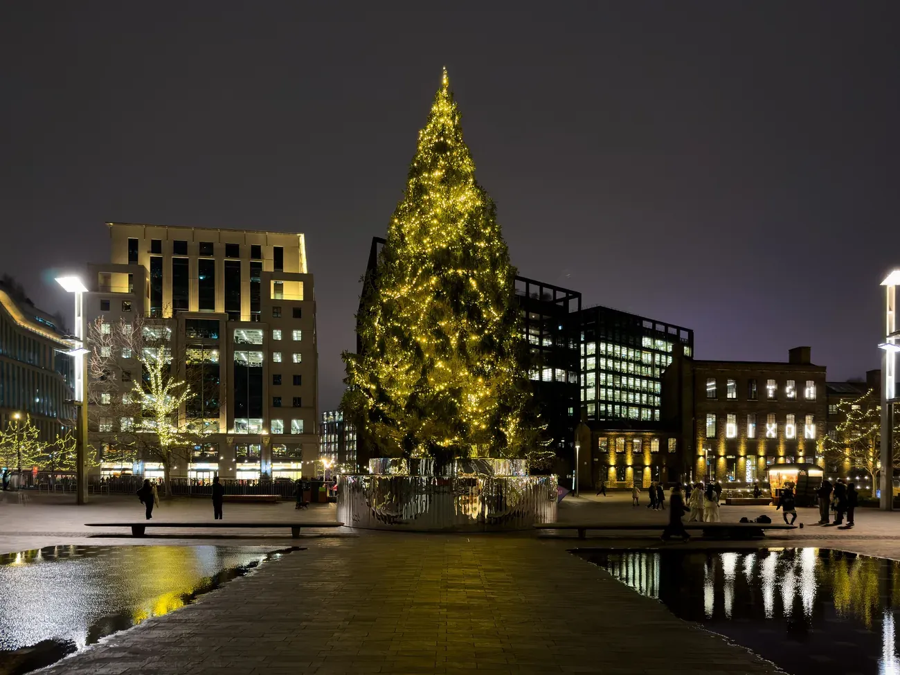 A tall Christmas tree covered in golden lights on Granary Square at King's Cross, London, at night