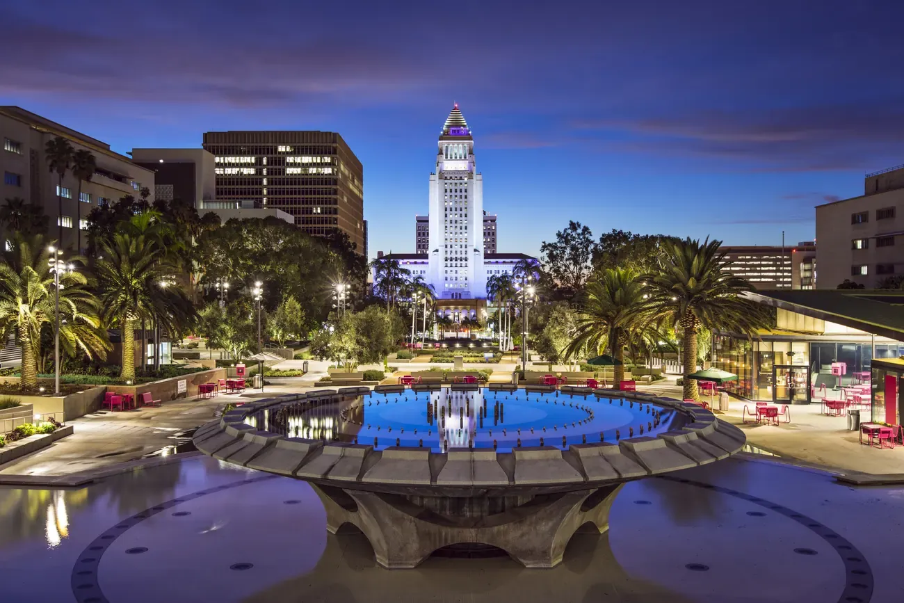 Los Angeles City Hall illuminated at dusk with the Grand Park fountain in the foreground