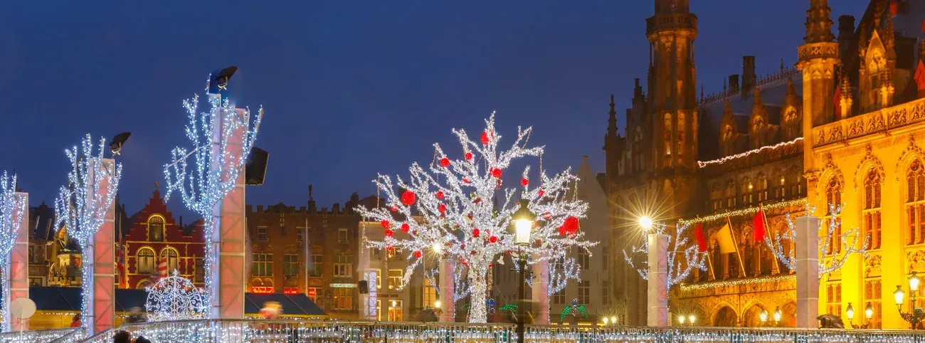 Trees of white lights on the Markt in Bruges in the evening, with the Provinciaal Hof and the guild houses behind