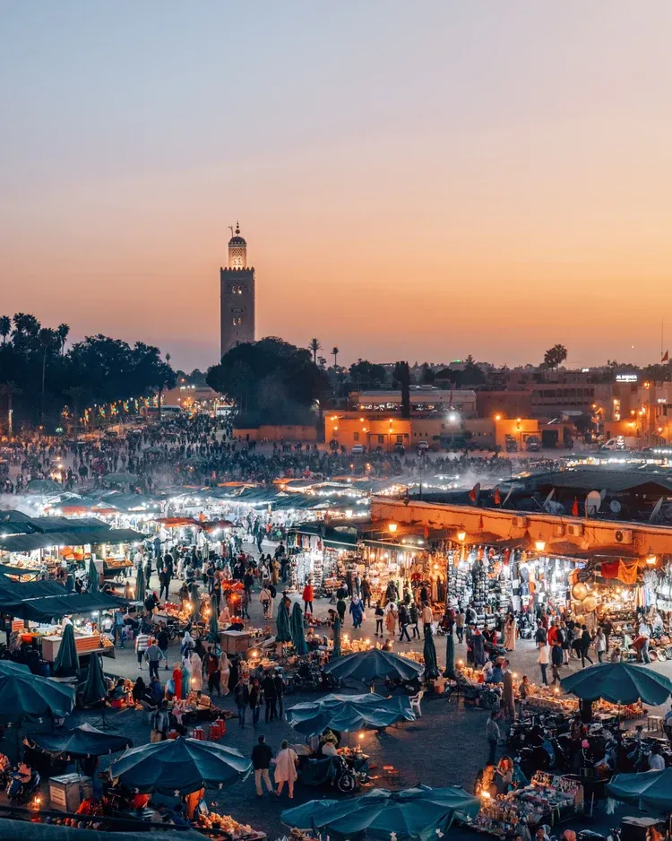 Food stalls filling Jemaa el-Fnaa at dusk with the Koutoubia minaret behind in Marrakech