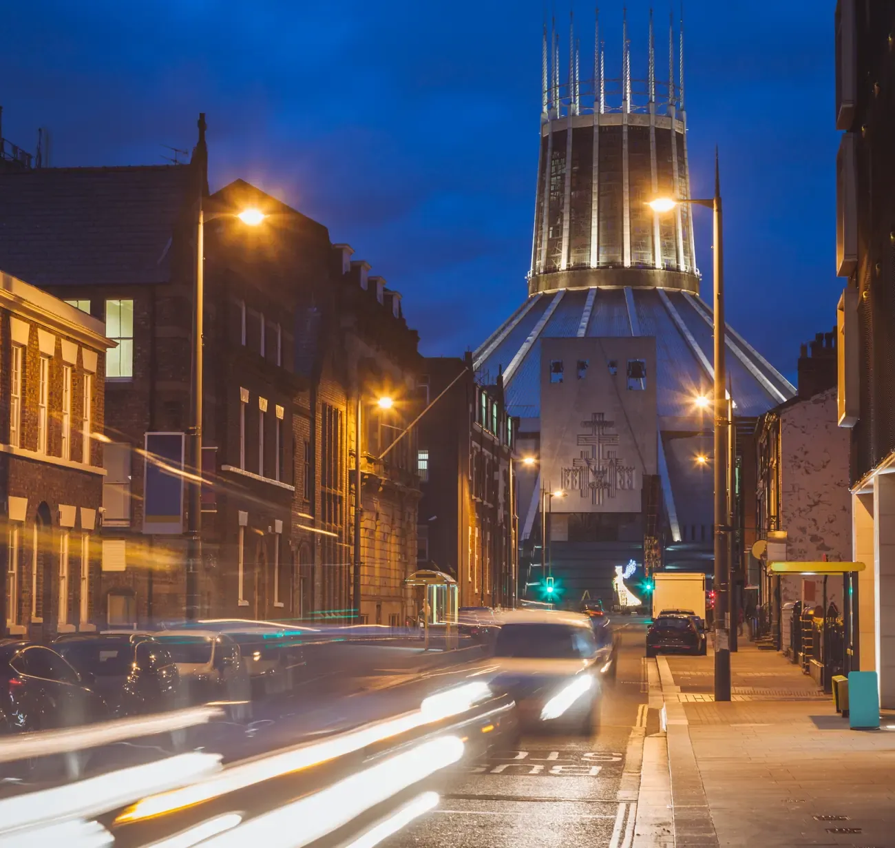 The lantern tower of Liverpool Metropolitan Cathedral lit at dusk at the end of a street with car light trails