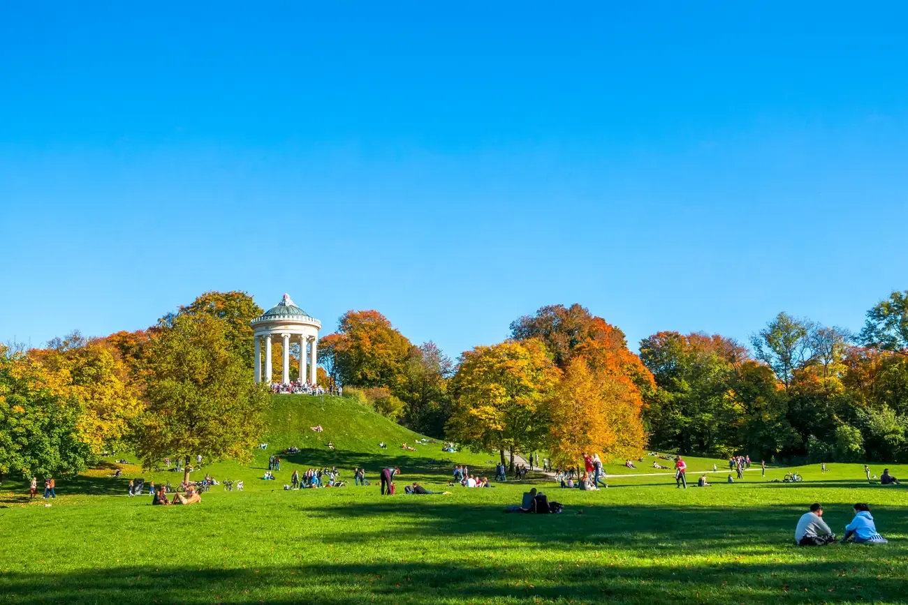 The Monopteros temple on its hill above people relaxing on the lawn in autumn in the Englischer Garten in Munich