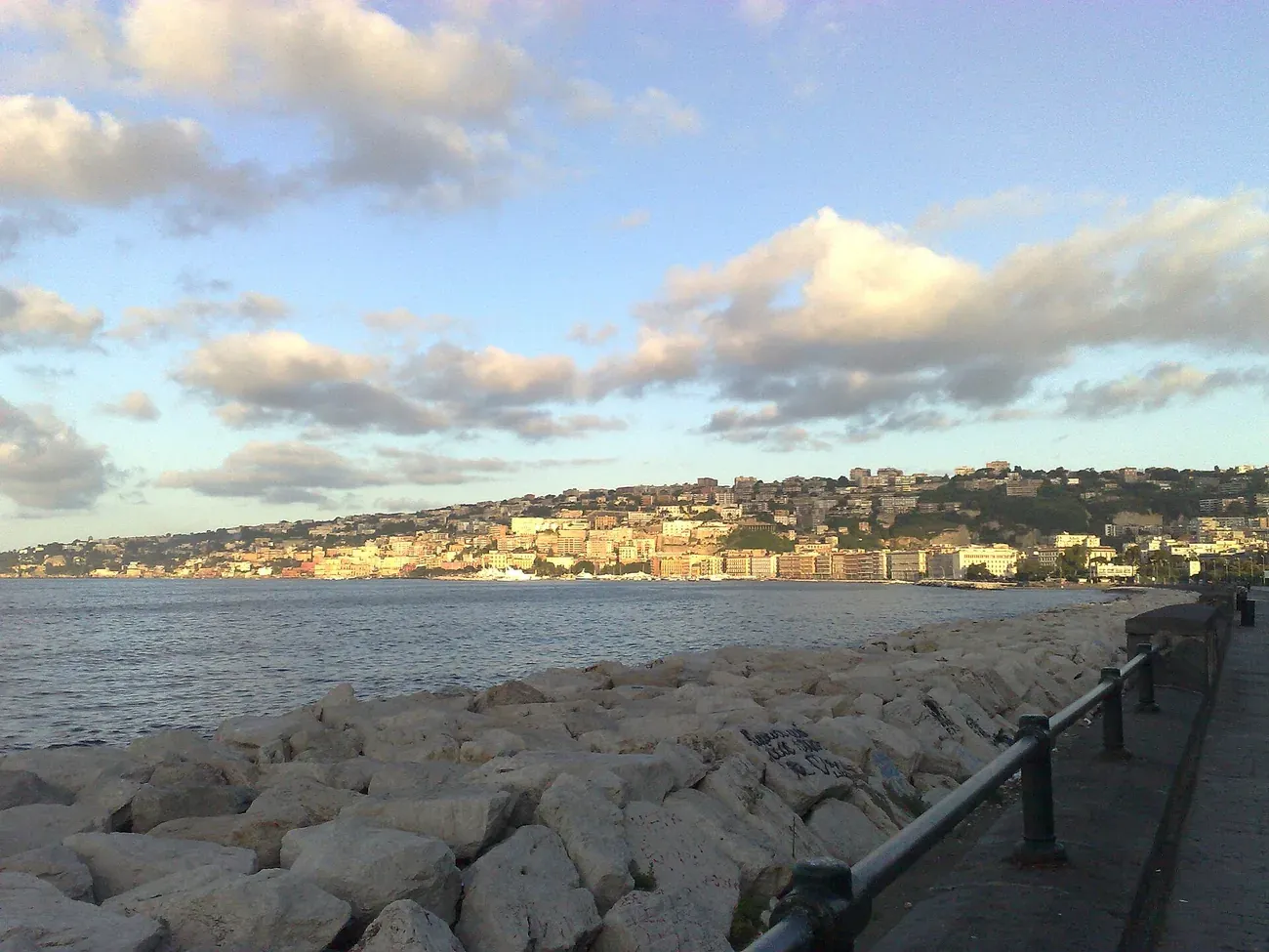 The seafront promenade along Via Caracciolo in Naples, with the sea wall, rocks and the Posillipo hill across the bay