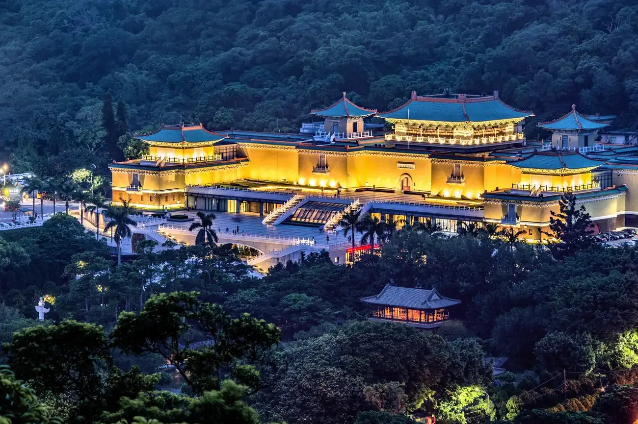 The National Palace Museum building lit on its wooded hillside at dusk, Taipei