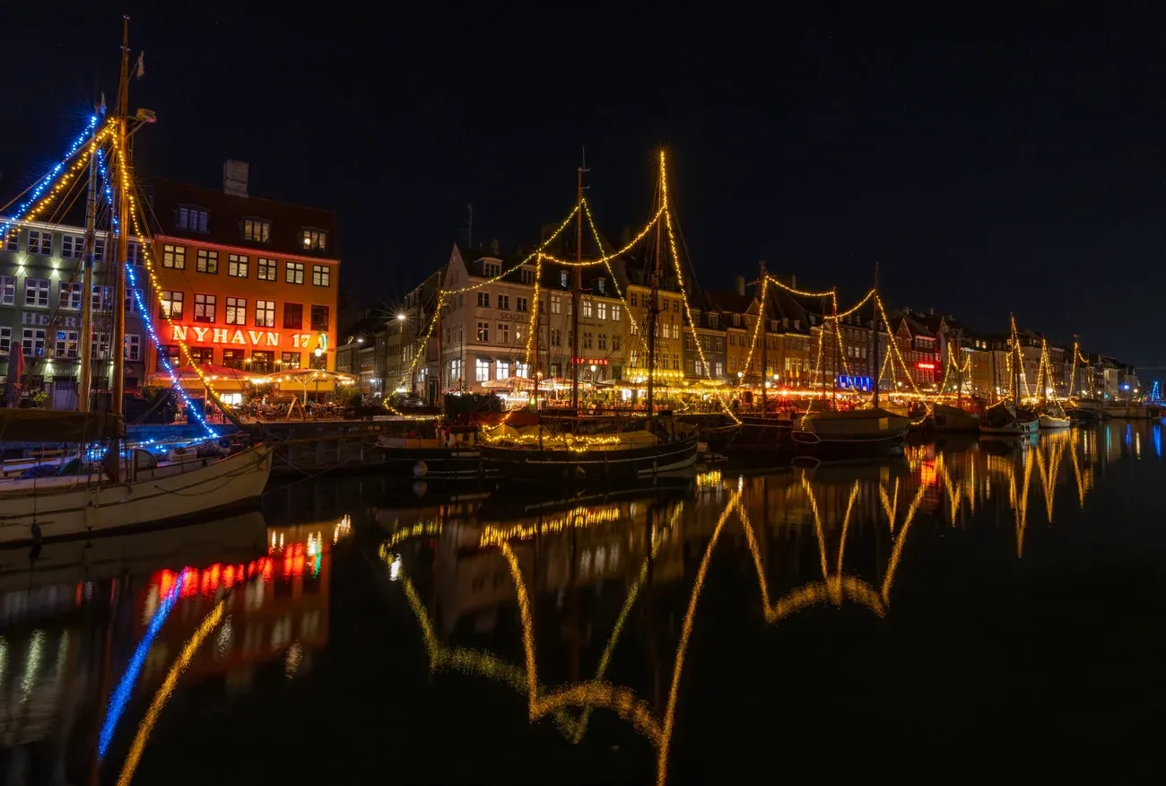 Nyhavn in Copenhagen at night, with lights strung along the masts of old ships and reflected in the canal