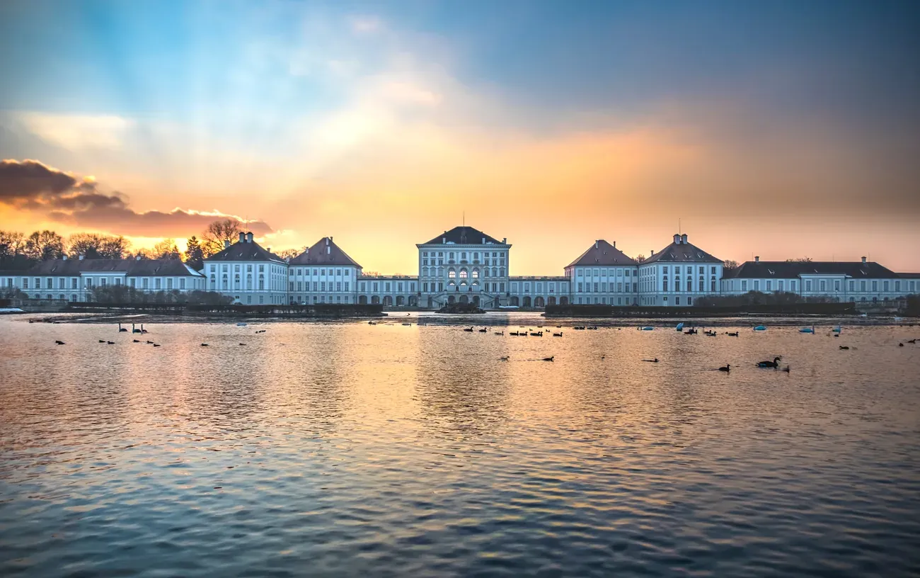Nymphenburg Palace seen across its canal at sunset with ducks on the water in Munich