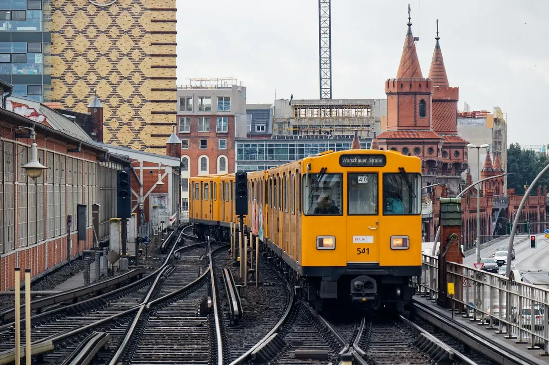 A yellow U-Bahn train on the elevated track approaching the towers of the Oberbaum Bridge in Berlin