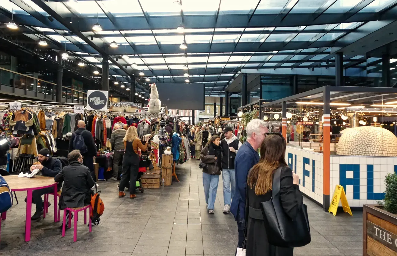 Clothing stalls and shoppers under the roof of Old Spitalfields Market, London