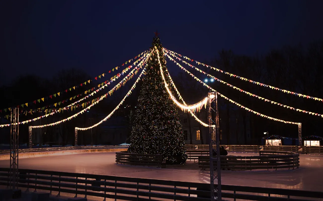 Outdoor ice rink with a lit Christmas tree and string lights at night