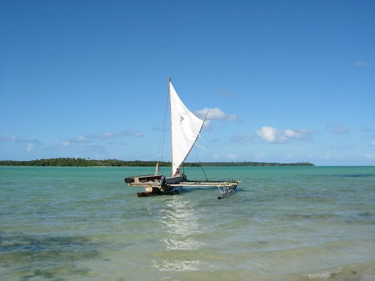 A traditional outrigger canoe under sail on the lagoon of the Isle of Pines, New Caledonia