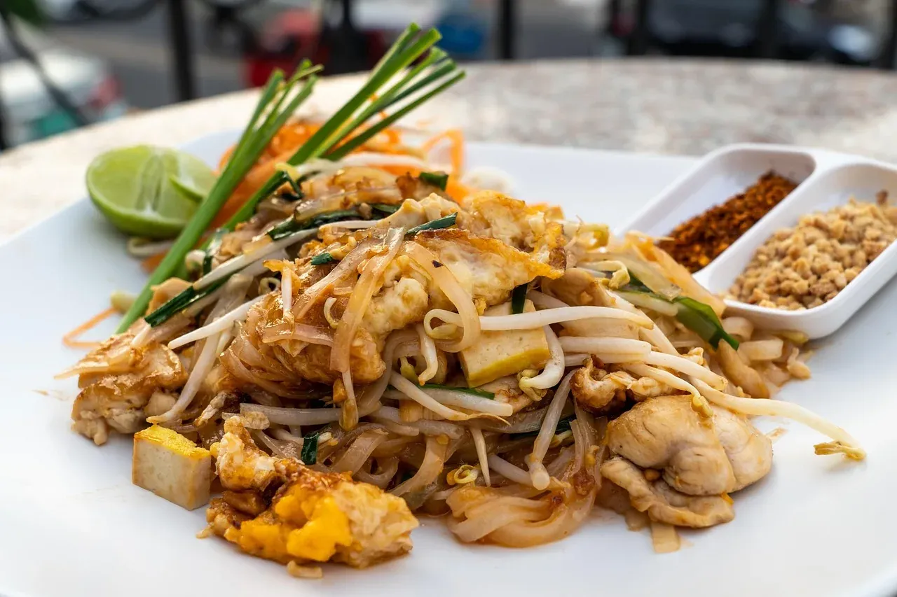 A plate of pad thai with bean sprouts, peanuts and lime