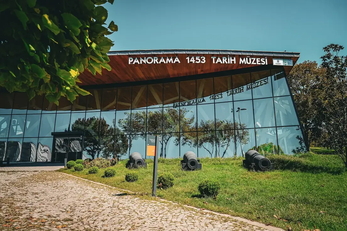 The glass and timber entrance building of the Panorama 1453 History Museum in Topkapı Cultural Park, Istanbul, with Ottoman cannons on the lawn