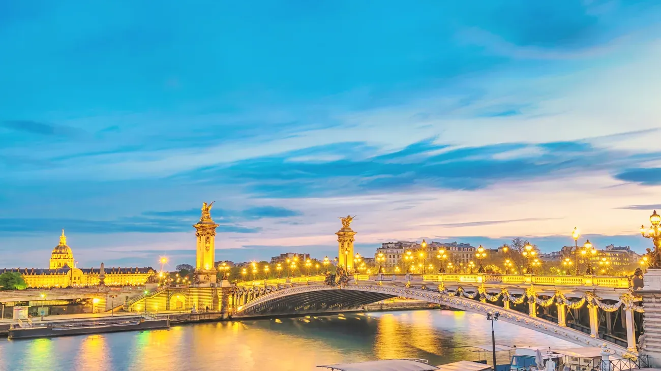 Pont Alexandre III lit up over the Seine at blue hour, with the dome of Les Invalides on the left