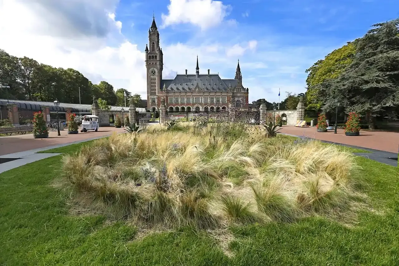 The brick facade and clock tower of the Peace Palace seen across its lawn in The Hague