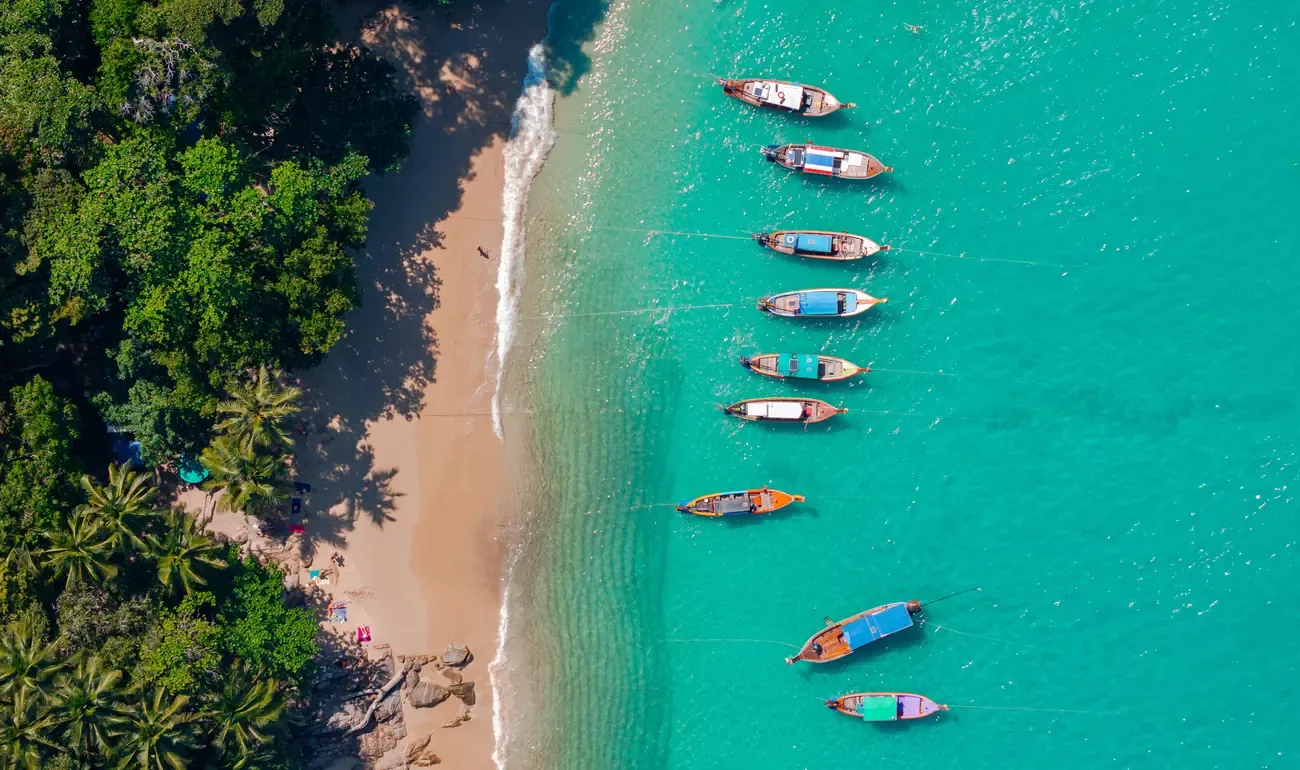Aerial view of a beach with longtail boats in clear turquoise water, Phuket