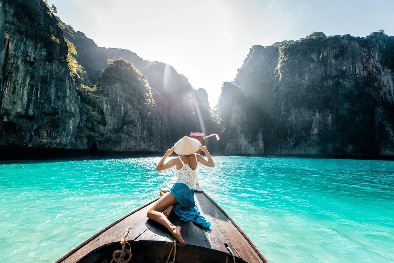 A woman on a longtail boat in a turquoise lagoon among cliffs, Phi Phi